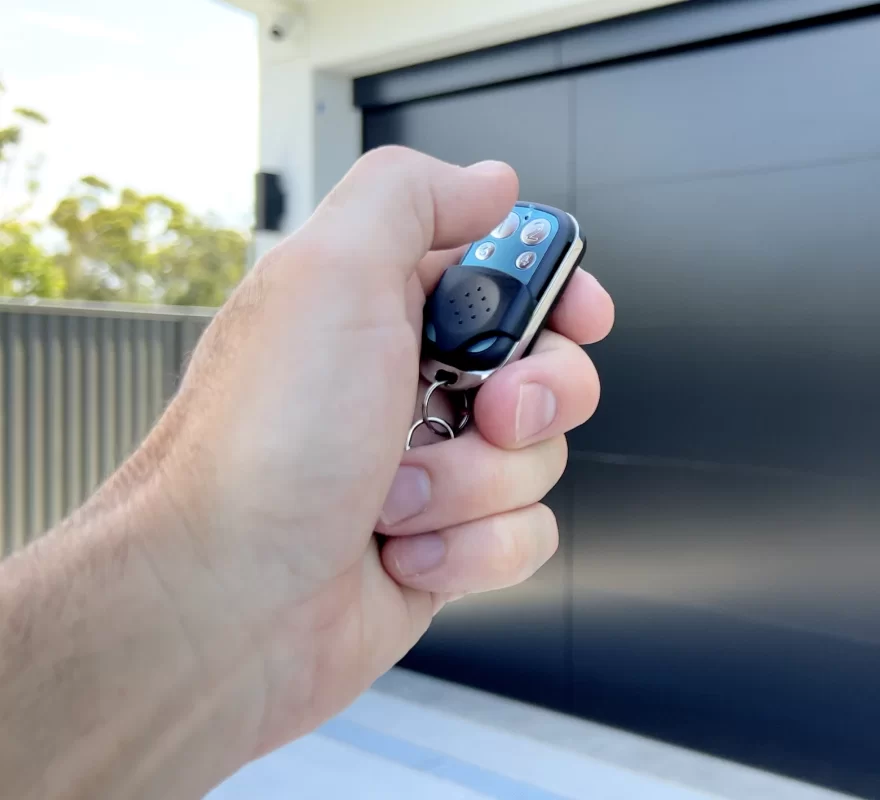 Hand holding a garage door remote control in front of a closed garage door